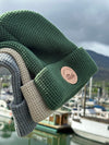 The three beanies are held out in front of the Juneau Boat Harbor