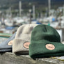 Green Cream and Gray boat beanies are displayed out in front of a boat harbor in Juneau