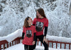 Two people wearing matching red shirts with bear graphics standing on a snow-covered deck.