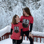 Two people wearing matching red shirts with bear graphics standing on a snow-covered deck.