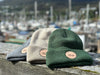 Green Cream and Gray boat beanies are displayed out in front of a boat harbor in Juneau